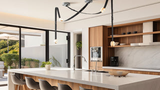 Modern kitchen interior with pendant LED lights over the countertop, surrounded by wooden cabinetry and white marble surfaces, with a view of a kitchen island and stools in the foreground.